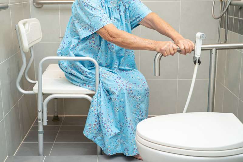 Persona mayor en silla de ducha utilizando barras de apoyo en baño adaptado