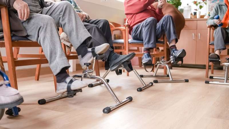 Personas mayores ejercitando las piernas con pedales estáticos en una sala de rehabilitación