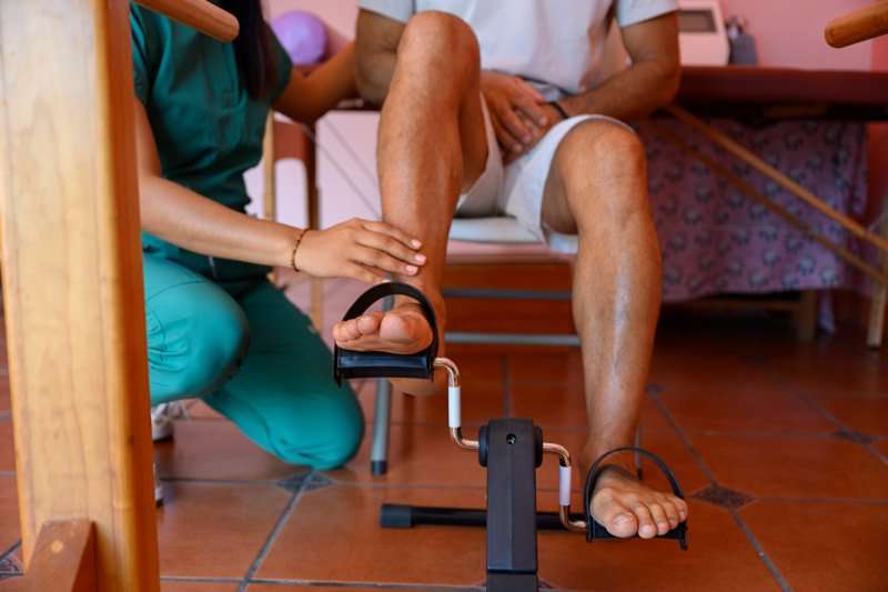 Fisioterapeuta ayudando a paciente a usar pedaleador durante la rehabilitación
