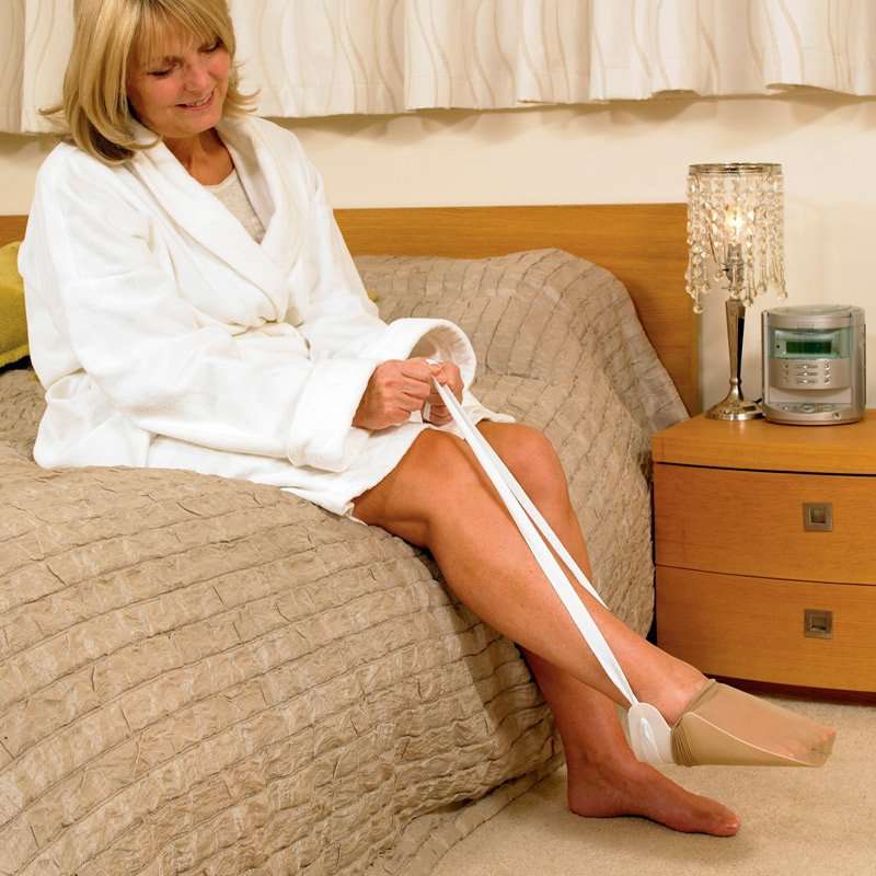 Mujer usando calzador de medias y calcetines sentada en la cama
