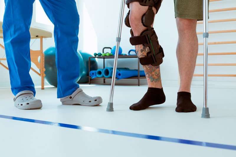 Persona con órtesis de rodilla caminando con muletas en rehabilitación