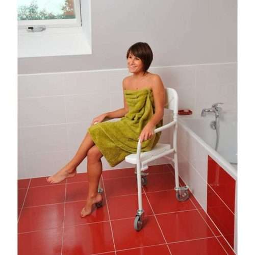 Persona sentada en la silla de ducha Tobago en versión con ruedas junto a la bañera