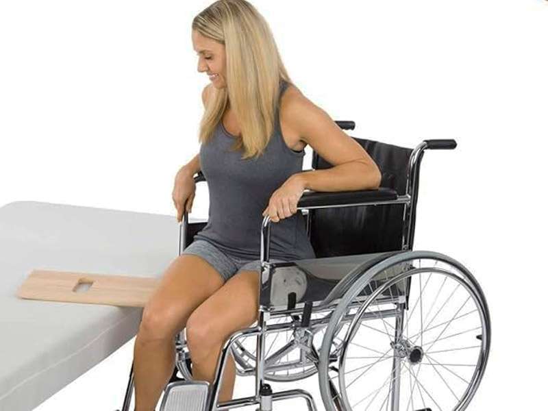 Mujer realizando una transferencia con tabla de madera desde silla de ruedas a cama