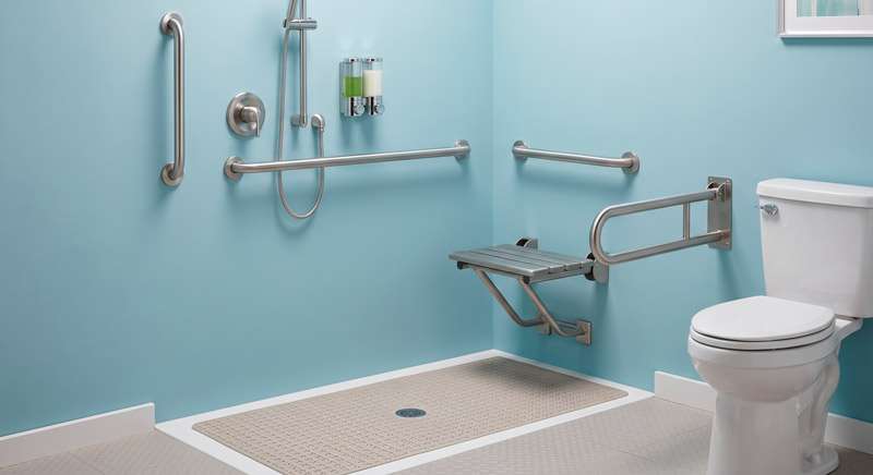 Baño adaptado con barras de apoyo, asiento abatible y superficie antideslizante