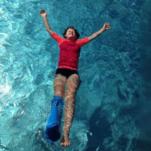 Niño con protector impermeable de escayola para pierna nadando en piscina